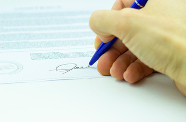 Businessman sitting at office desk signing a contract with shallow focus on signature.