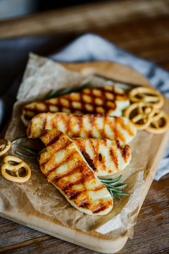 fried halloumi cheese with rosemary on a wooden cutting board on wooden table with small pretzels