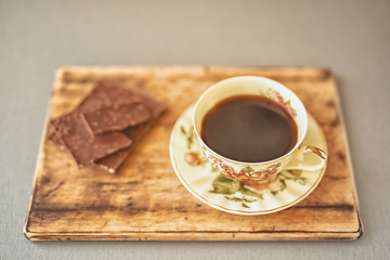 a beautiful coffee Cup with a picture of roses on a wooden stand against a background of chocolate pieces