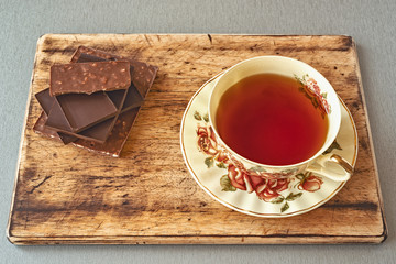 beautiful Cup of tea with the image of roses on a wooden stand against the background of pieces of chocolate