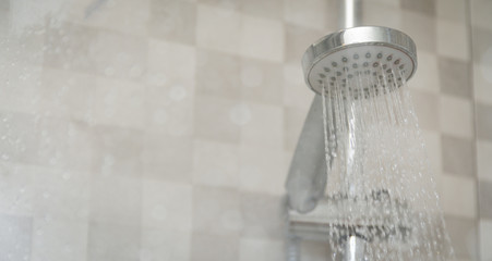 Naklejka na ściany i meble Fresh shower behind wet glass window with water drops splashing. Water running from shower head.