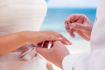 Bride and groom exchanging wedding rings close up during symbolic nautical decor destination wedding marriage on sandy beach in front of the ocean in Punta Cana, Dominican republic  