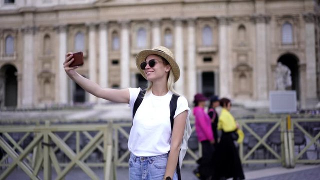 Happy female tourist in stylish sunglasses enjoying trip to Roma making photo via modern cellular phone camera, smiling hipster girl posing for selfie images via app during summer vacations holidays
