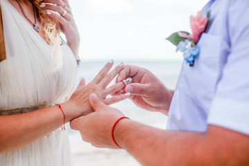 Bride and groom exchanging wedding rings close up during symbolic nautical decor destination wedding marriage on sandy beach in front of the ocean in Punta Cana, Dominican republic  