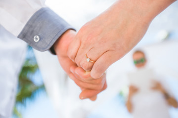 Bride and groom exchanging wedding rings close up during symbolic nautical decor destination wedding marriage on sandy beach in front of the ocean in Punta Cana, Dominican republic  