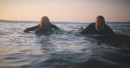 Senior man and woman surfing in the water at sunset - Powered by Adobe