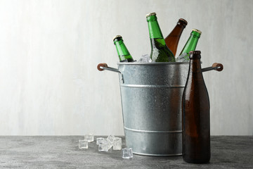 Metal bucket with beer and ice cubes on grey background. Space for text