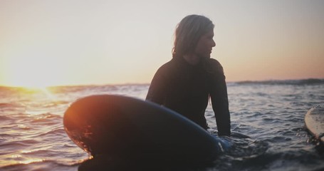 Close up senior woman surfing in the water at sunset