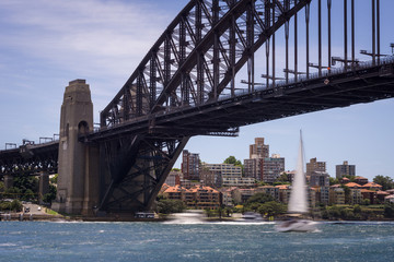 Naklejka premium Sailboat crossing under the Sydney Harbor Bridge on a sunny day at circular quay in Sydney, Australia