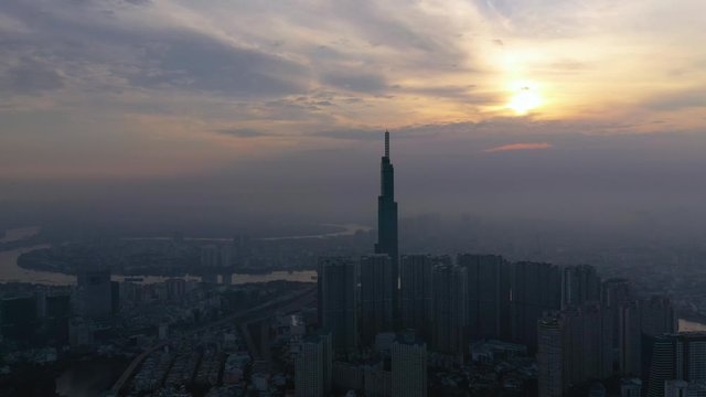 Sunrise with smoggy morning panoramic drone shot over densely populated urban area of a modern city with high rise towers in silhouette. camera is tracking left to right
