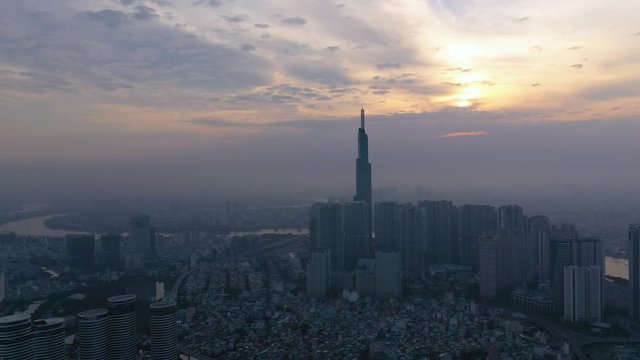 Sunrise with smoggy morning panoramic drone shot over densely populated urban area of a modern city with high rise towers in silhouette. upward crane shot revealing the river
