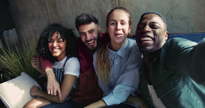 Multi-ethnic young friends smiling taking selfie on sofa