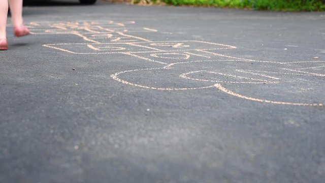 little kid playing hopscotch outside in driveway in spring