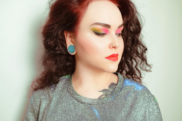 Photo of a girl portrait of a brunette with color makeup, shades of red, green, yellow. Gorgeous professional bright makeup. Girl with a tunnel in the ear. Gorgeous make-up model.