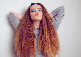 Girl with curled voluminous hair, model with hairstyle in the style of the 80s. 90s, with bright blue make-up. Hair care, brunette red-haired girl with long hair, curling curls, corrugation hair