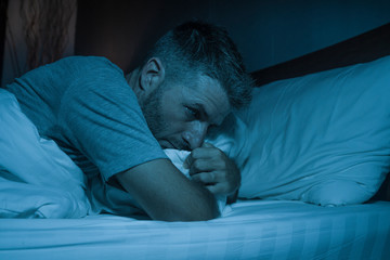 dramatic portrait in the dark of attractive depressed and worried man on bed suffering depression crisis and anxiety feeling lost lying sleepless in insomnia and life problem concept - obrazy, fototapety, plakaty
