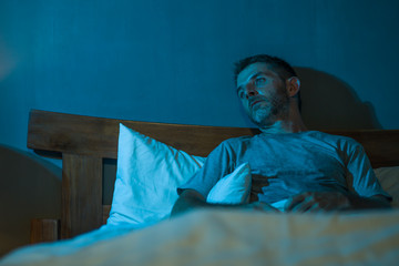 dramatic portrait in the dark of attractive depressed and worried man on bed suffering depression...