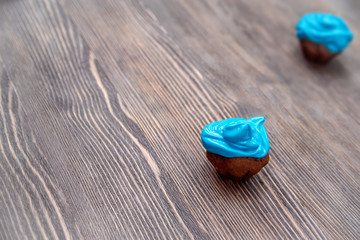 two small homemade chocolate cupcakes with blue cream on a wooden table