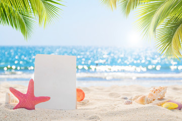 Fototapeta na wymiar Sandy beach with empty paper card for message design. blur sea on background. Tranquil beach scene for travel inspirational. Summer exotic holiday and vacation concept for tourism relaxing.