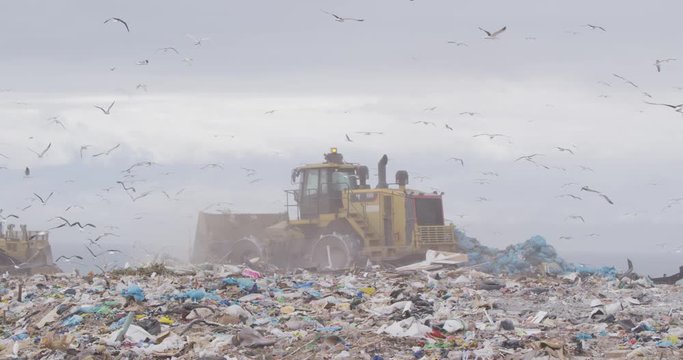 Vehicles clearing rubbish piled on a landfill full of trash 