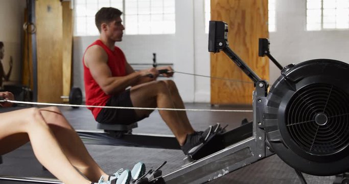 Side view athletic Caucasian friends exercising on a rowing machine