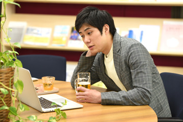 パソコンを見ながらビールを飲む男性