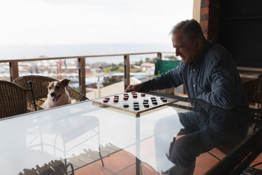 Senior Man Playing Checkers On His Terrace 