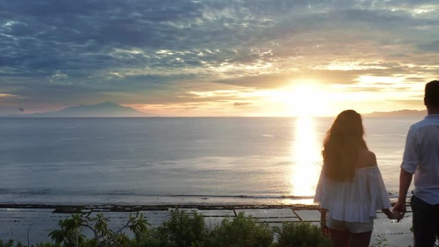 Couple In Love At Luxury Resort On Romantic Summer Vacation. People Relaxing Together In Edge Swimming Pool , Enjoying Beautiful sunset Sea View. Happy Lovers On Honeymoon Travel. Relationship, Romanc