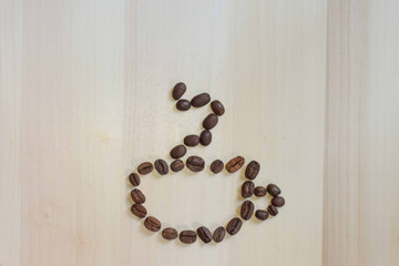 Roasted coffee beans forming a coffee mug with smoke on a wooden texture background with copy space. Coffee mug on top of the coffee beans.