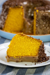 delicious piece of carrot cake with brigadeiro topping (Brazilian chocolate and milk sweet), on a white plate with the cake in the background on top of a blue cloth