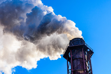 View on smoke pipe of the factory against blue sky. Environmental pollution