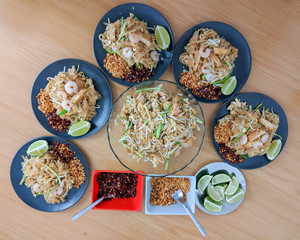Table setting for five individuals. Serving freshly cooked pad Thai with lemon, chili and ground peanuts as side dish.