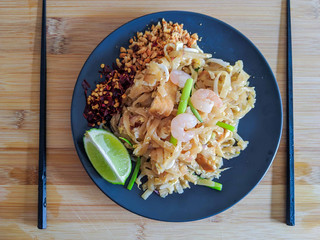 shrimp pad thai on plate in flat lay composition with copy space atop rustic wooden table. Pad Thai with chilli, lemon and ground nuts on the side dish. 