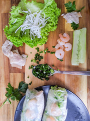 Fresh Spring Roll on a black plate with green lettuce, cucumber, basil leaves, white noodles and shrimps, Vietnamese Food. Spring rolls on wooden texture background.