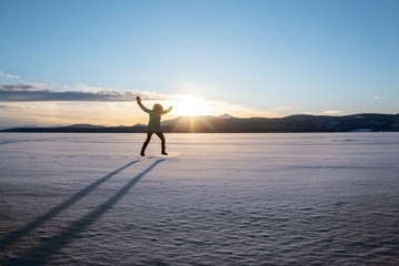 Silhouette of person woman jumping on frozen lake at sunset with mountains in the background. 