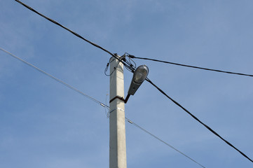 Iron-concrete lighting pole with a lantern and wires against a blue sky.
