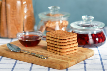 A stack of shortbread cookies on a wooden tray against the background of glass cans of biscuits and against the background of a glass jar of jam
