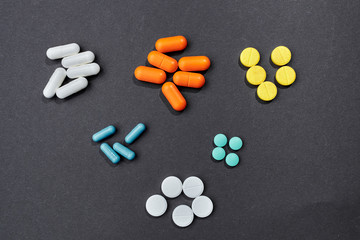 several handfuls of multicolored tablets lie in a row against a gray background. top view