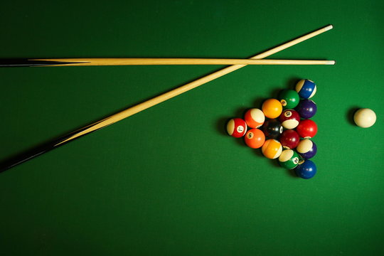 backdrop of pyramid of pool balls and billiard cues on green billiard table