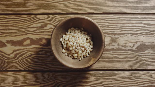 TOP VIEW: Peeled pine nuts fill wooden cup. Stop motion