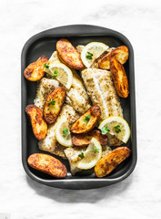 Baked fish fillet and potatoes on a baking sheet on a light background, top view. Mediterranean style lunch