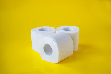 Three rolls of white toilet paper on a yellow background