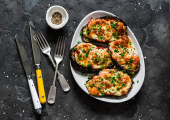 Baked eggplant with ham, tomatoes and mozzarella - delicious appetizer, tapas on a dark background, top view