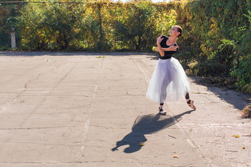 Fototapeta premium Woman ballerina in a white ballet skirt dancing in pointe shoes in autumn park.