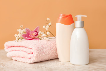 Fototapeta na wymiar Shower gels, towel and flowers on color background