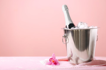 Bucket with ice and champagne on color background