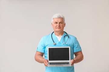 Mature male doctor with laptop on grey background