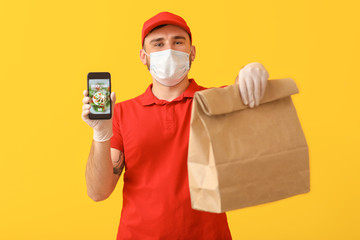 Fototapeta na wymiar Male courier of food delivery company in medical mask and with mobile phone on color background