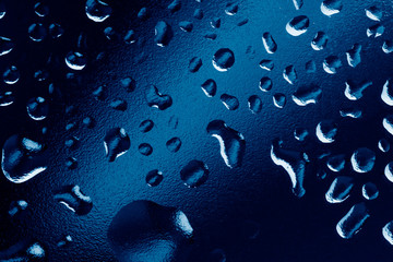 Water drops on window glass. Rain drops on dark trendy blue background. Macro, closeup.