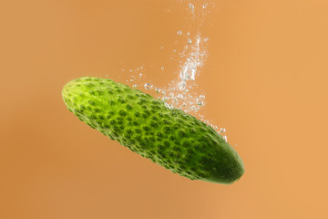 Falling of fresh cucumber into water against color background
